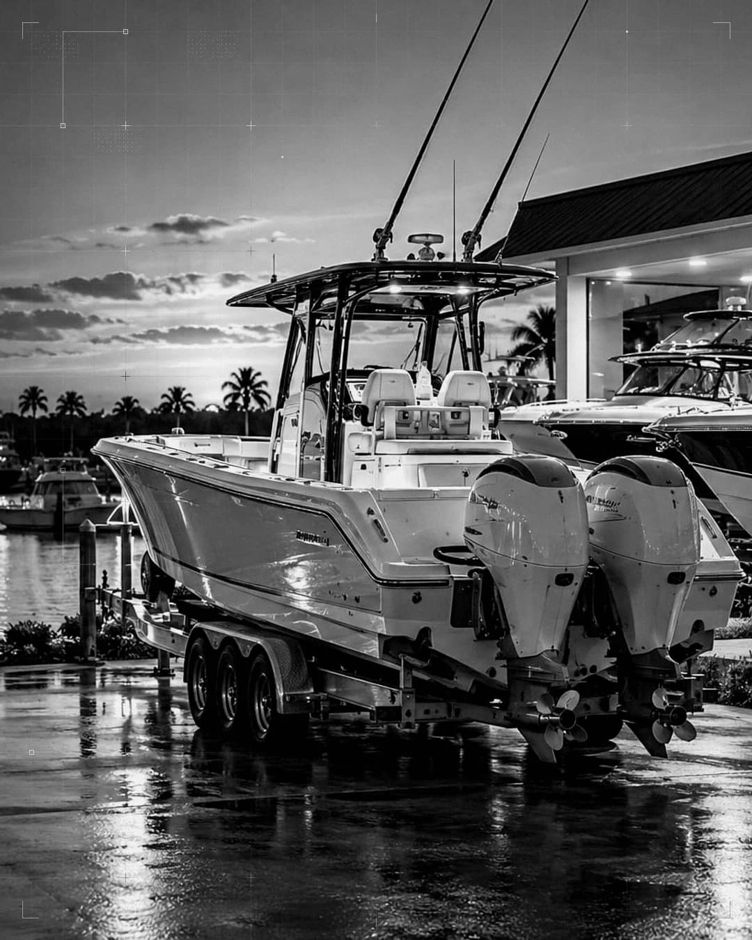 A center-console boat with twin outboards on a trailer at a marina, boats in the slips behind it.