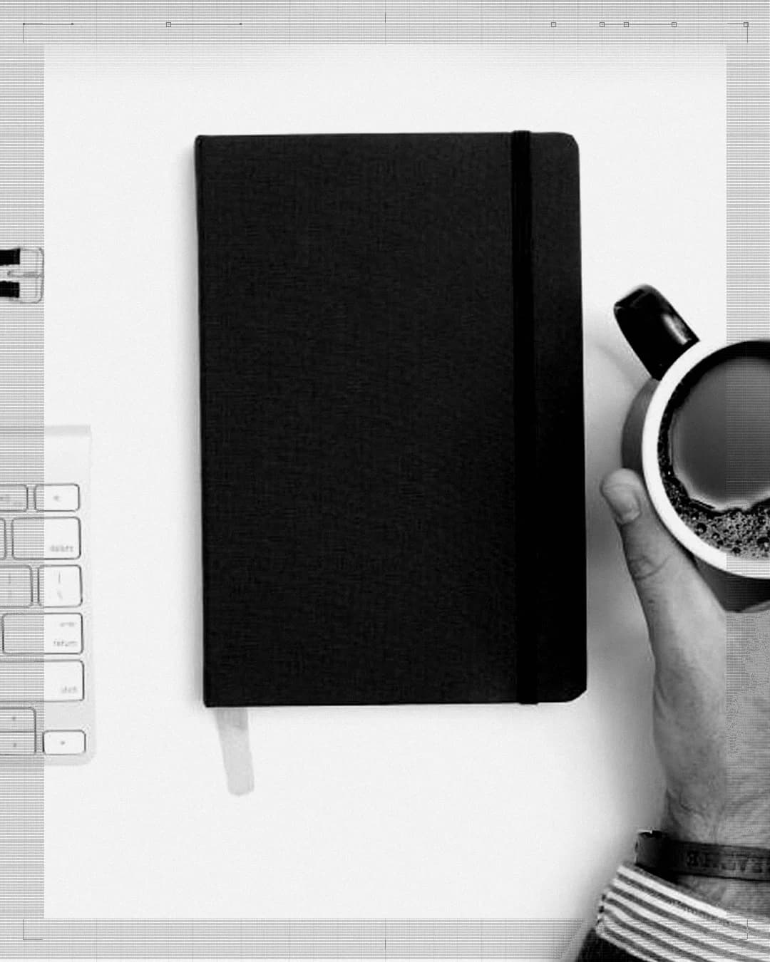Hands at a keyboard beside a closed notebook and a cup of coffee on a white desk.